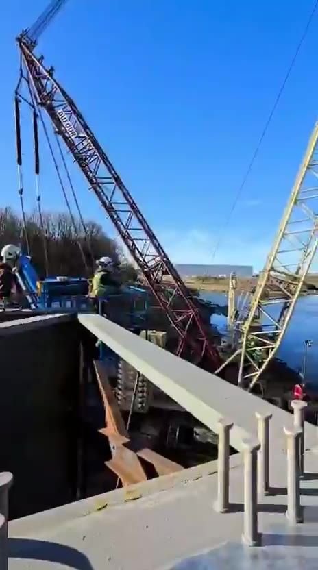 Montaj cu macarale pe șenile lângă tablier, peste apă.